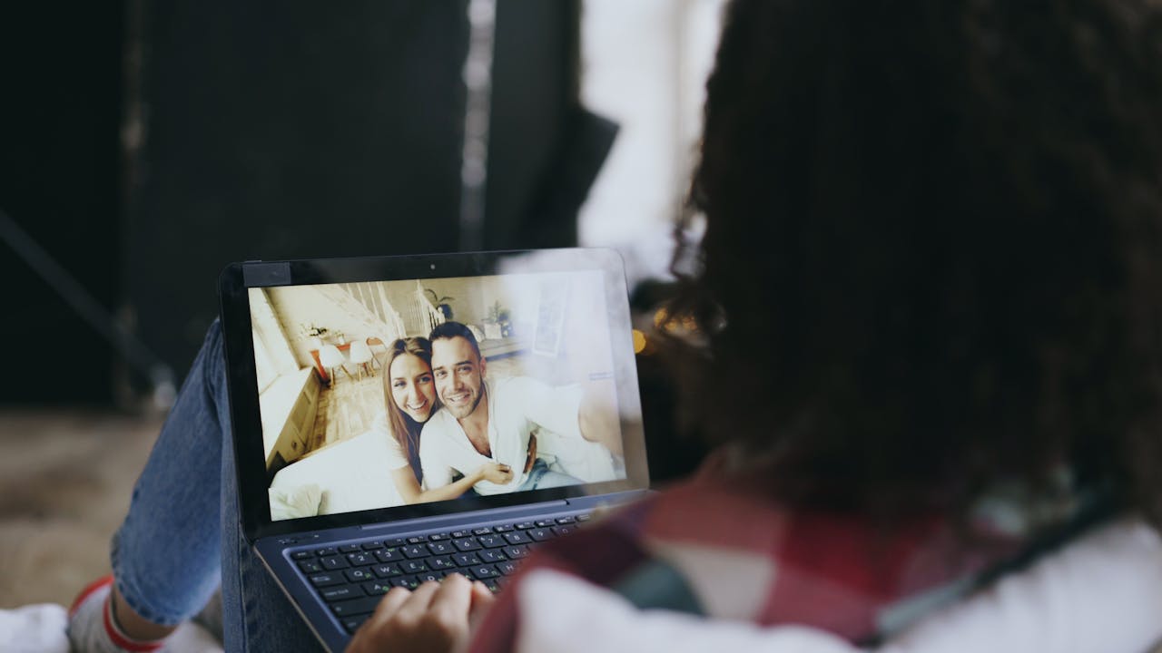 Woman viewing a happy couple's photo on a laptop at home, suggesting connection through technology.