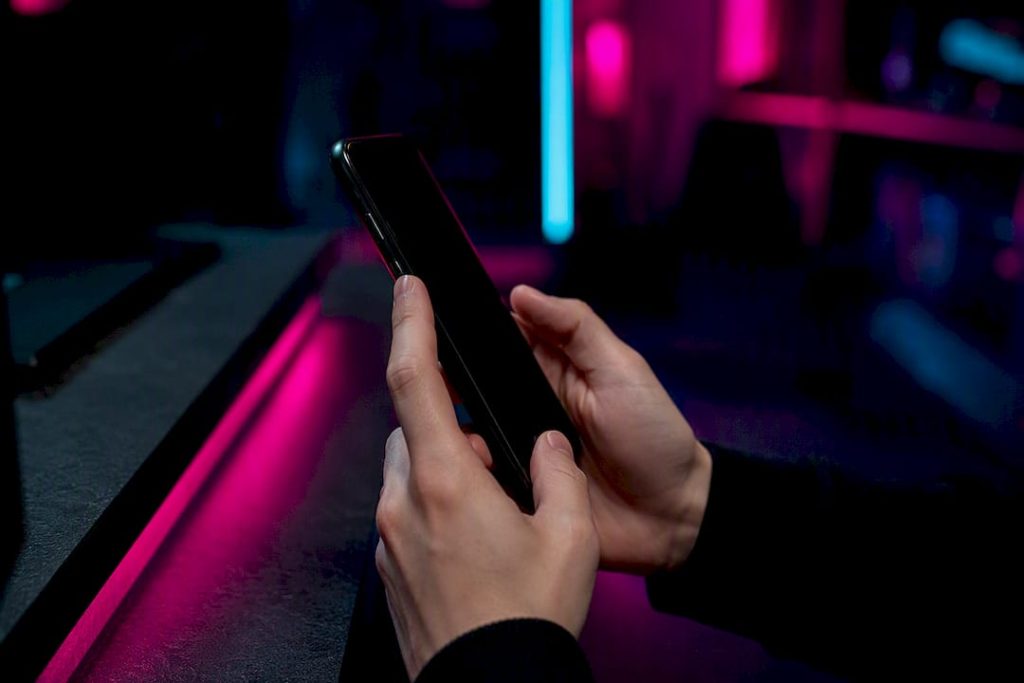 Hands adjusting smartphone in neon-lit room